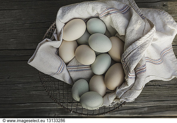 Overhead view of eggs on textile in basket at wooden table