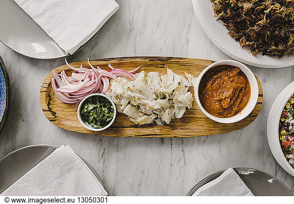 Overhead view of fish with onions and curry in wooden tray on table