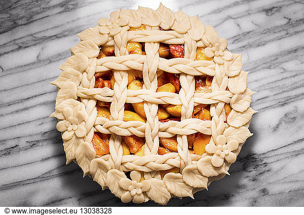 Overhead view of floral peach pie on marble counter