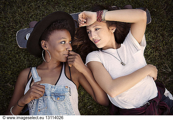 Overhead view of friends resting head on skateboard while lying on grassy field