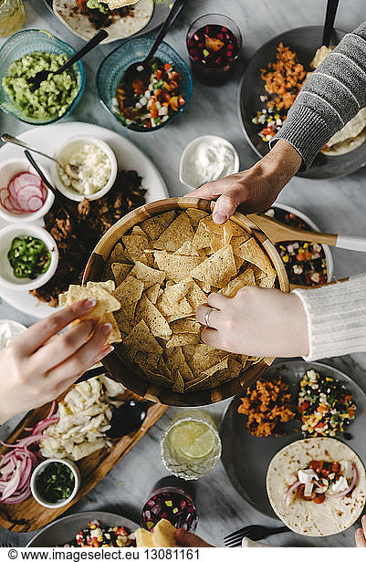 Overhead view of friends taking nacho chips while having food at table during social gathering