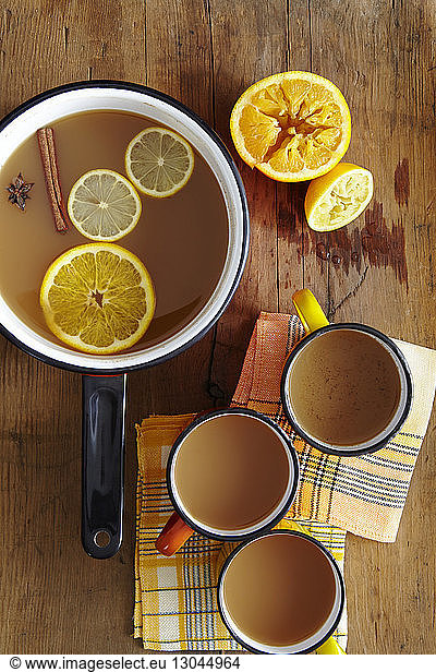 Overhead view of hot apple cider in saucepan and mugs on wooden table
