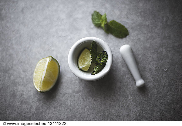 Overhead view of lemon and mint leaves in mortar by pestle on kitchen counter