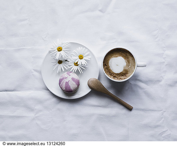 Overhead view of macaroon with daisies in plate by coffee on white textile