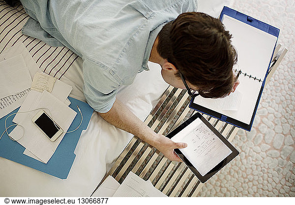 Overhead view of man using tablet computer while working on bed at home