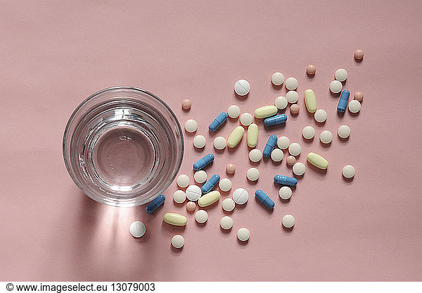 Overhead view of medicines with drinking water in glass over coral background
