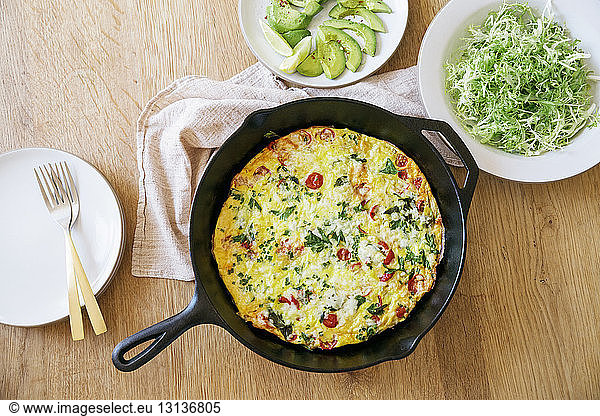 Overhead view of omelet in cooking pan with salad on table