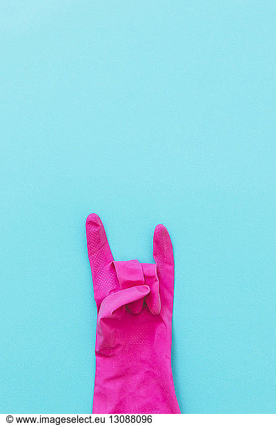 Overhead view of pink glove with horn sign on blue background