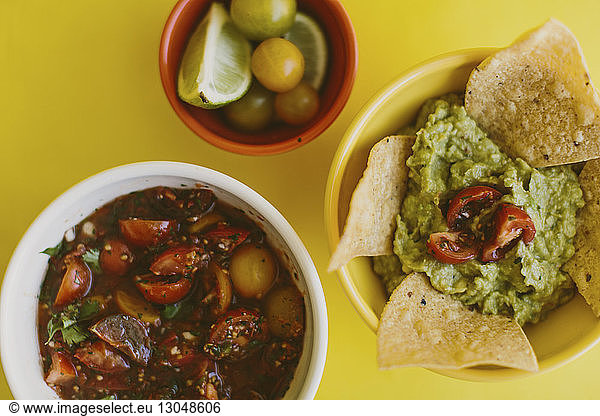 Overhead view of salsa and guacamole served with ingredients on yellow background