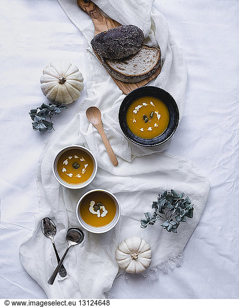 Overhead view of soup served in bowls with pumpkins and breads on textile