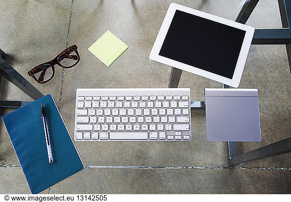 Overhead view of tablet computer with keyboard and touch pad on glass table in creative office