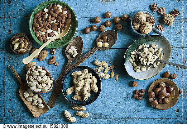 Overhead view of various nuts in bowls and on spoons on blue rustic table