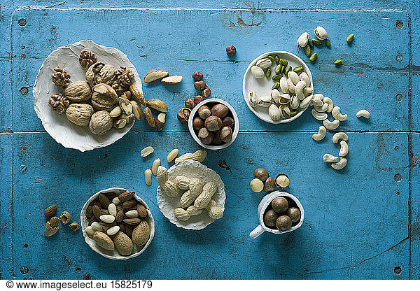 Overhead view of various nuts in bowls on blue rustic table