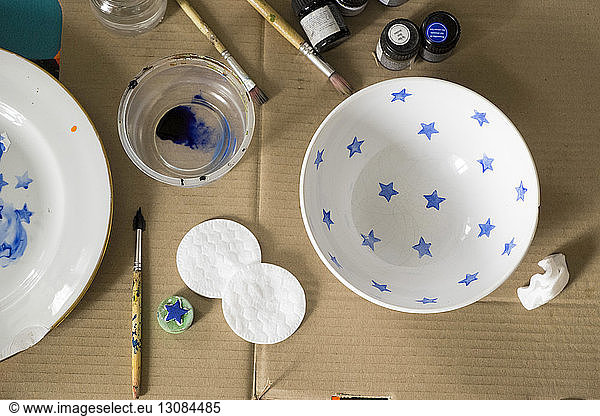 Overhead view of watercolor paints and brushes with bowls on cardboard