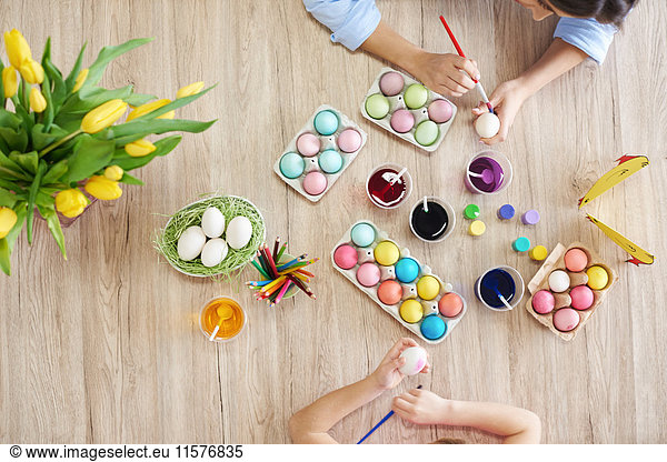 Overhead view of woman and daughter's hands painting easter eggs at table