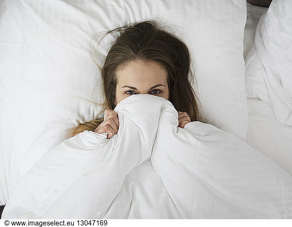 Overhead view of woman hiding in blanket on bed