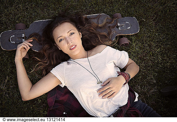 Overhead view of woman resting head on skateboard while lying on grassy field