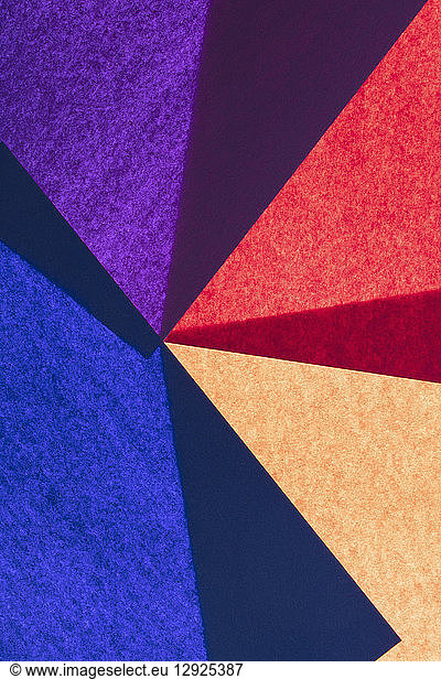 Overlapping pieces of multi-coloured construction paper on illuminated backdrop.