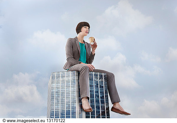 Oversized businesswoman sitting on skyscraper  low angle view