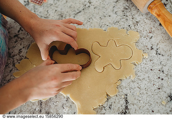 Overview of girl hands cutting out a cookie with cookie cutter