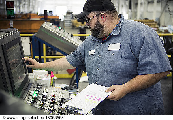 Overweight manual worker operating machinery at control panel in metal industry