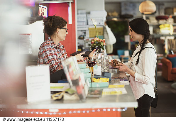 Owner showing drinking glasses to customer while standing at checkout counter in store