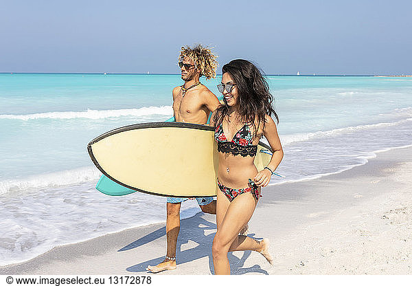 Paar  das am Strand läuft und Surfbretter trägt