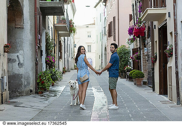Paar hält sich an den Händen und steht neben einem Hund auf dem Gehweg