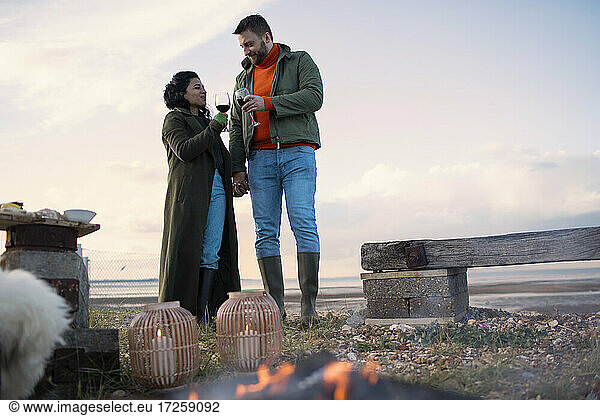 Paar in Wintermänteln genießt Rotwein am Strand