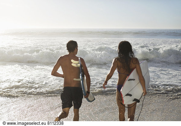 Paar läuft mit Surfbrettern in Richtung Ozean