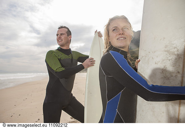 Paar mit Surfbrettern am Strand  die sich umsehen