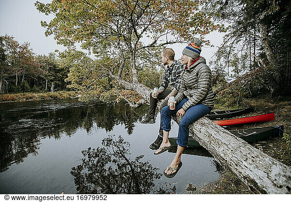 Paar sitzt auf einem Ast und trinkt Bier beim Kanufahren auf einem Fluss  Maine