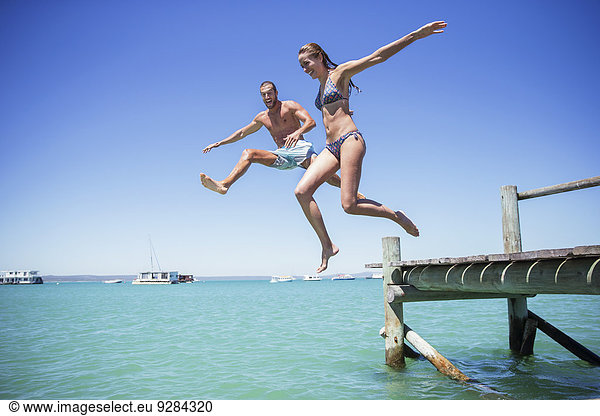 Paar springt vom Holzsteg ins Wasser