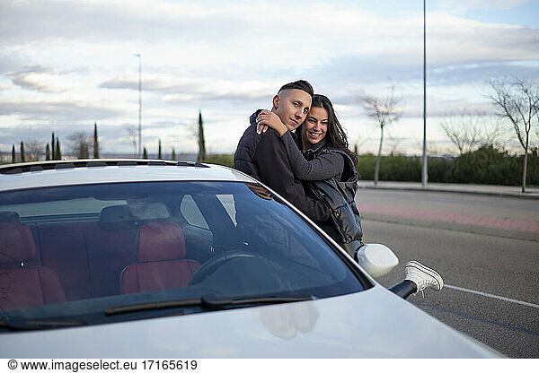 Paar umarmt sich  während es sich an ein Auto lehnt