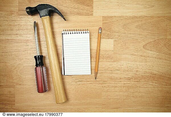 Pad of paper  pencil  hammer and screwdriver on a wood background