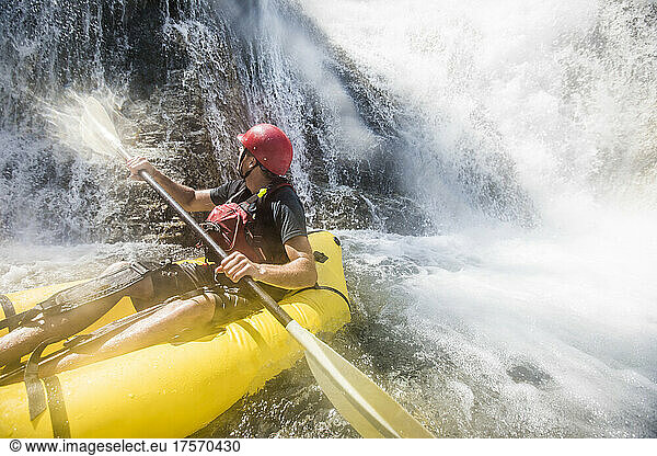 Paddler gets soaked while exploring river and waterfalls on raft.