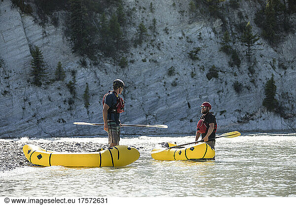 Paddlers stop to communicate and rest at rivers edge in canyon.