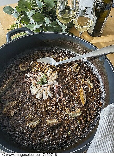 Paella mit Tintenfisch  Artischocken und Steinpilzen  dazu zwei Gläser Weißwein.