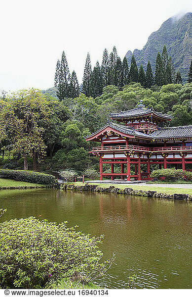 Pagoda on verge of pond with mountain behind.