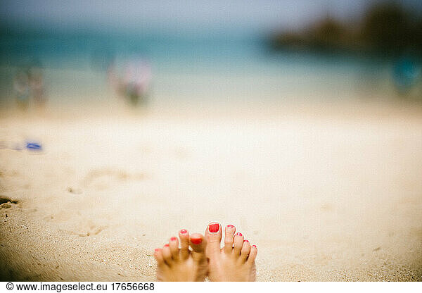 Painted toes on a white sand beach by the ocean