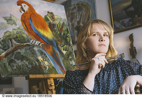 Painter holding paintbrush in front of bird painting