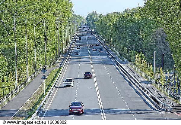 Panorama der Autobahn mit grünen Bäumen und Sträuchern am Rande. Schöne Straße und Bäume an den Seiten. Ökologie in der Stadt. Breite Asphaltstraße Autobahn Straße mit Laternen auf der Seitenlinie. Autobahn in der Nähe von Stadt.