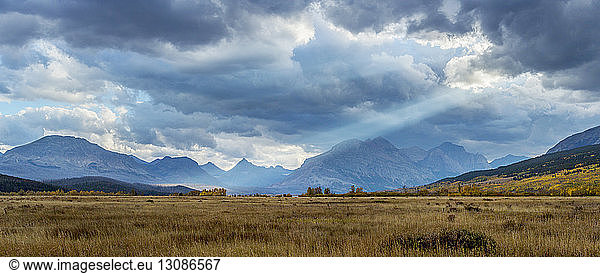 Panoramic view of grassy field and mountains against cloudy sky