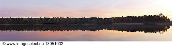 Panoramic view of lake by trees against sky during sunset