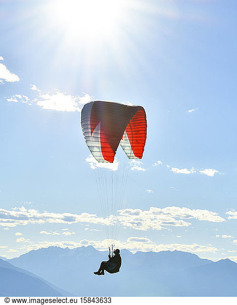 Paraglider flying in blue skies with sunflare