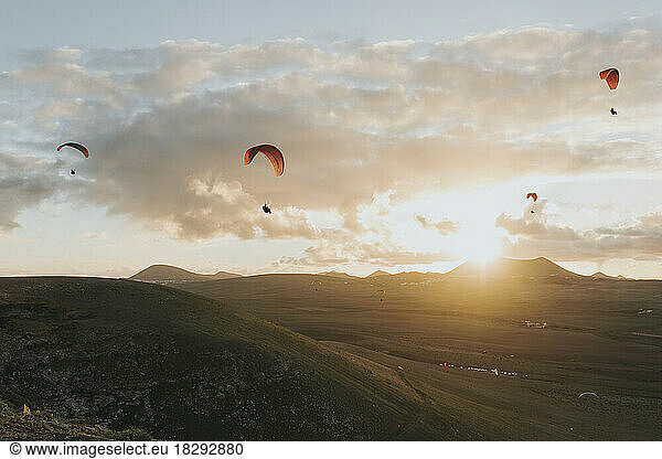 Paragliders flying under cloudy sky at sunset
