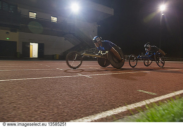 Paraplegic athletes speeding along sports track in wheelchair race at night
