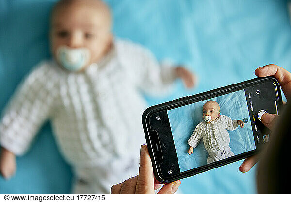 Parent taking photograph of baby lying down using smart phone  shot from above