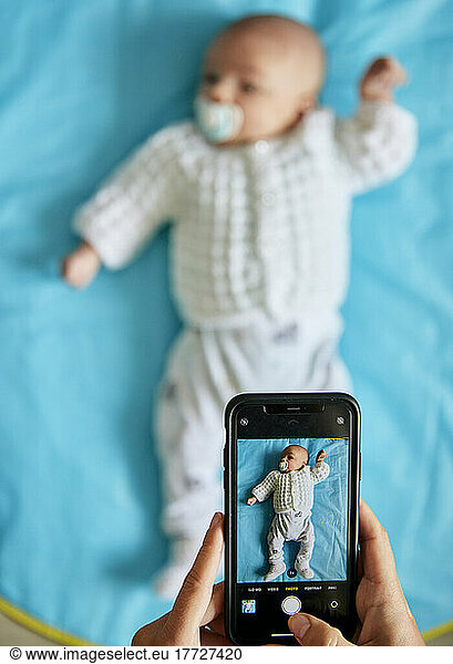 Parent taking photograph of baby lying down using smart phone  shot from above