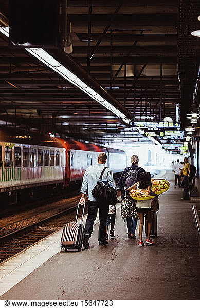 Parents and children walking with luggage on railroad station platform